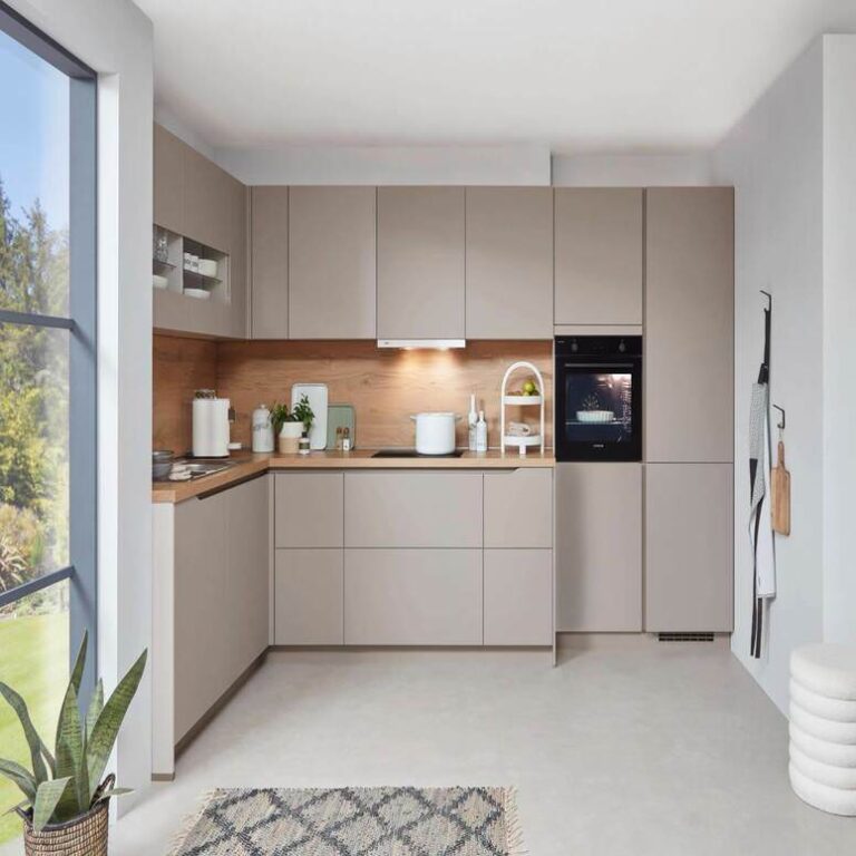 Musterküche in Kaschmir als L-Küche mit Holzrückwand und Backofen im Hochschrank – Küchenstudio Heidelberg